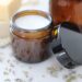 Cream lotion in a small amber glass jar with the lid leaning against it.