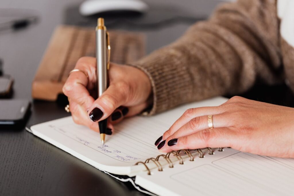 A lady holding a pen and starting to write in a journal.