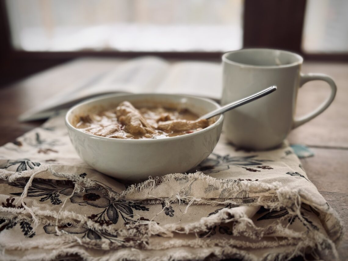A bowl of soup and a cup of tea sitting on a table with a book