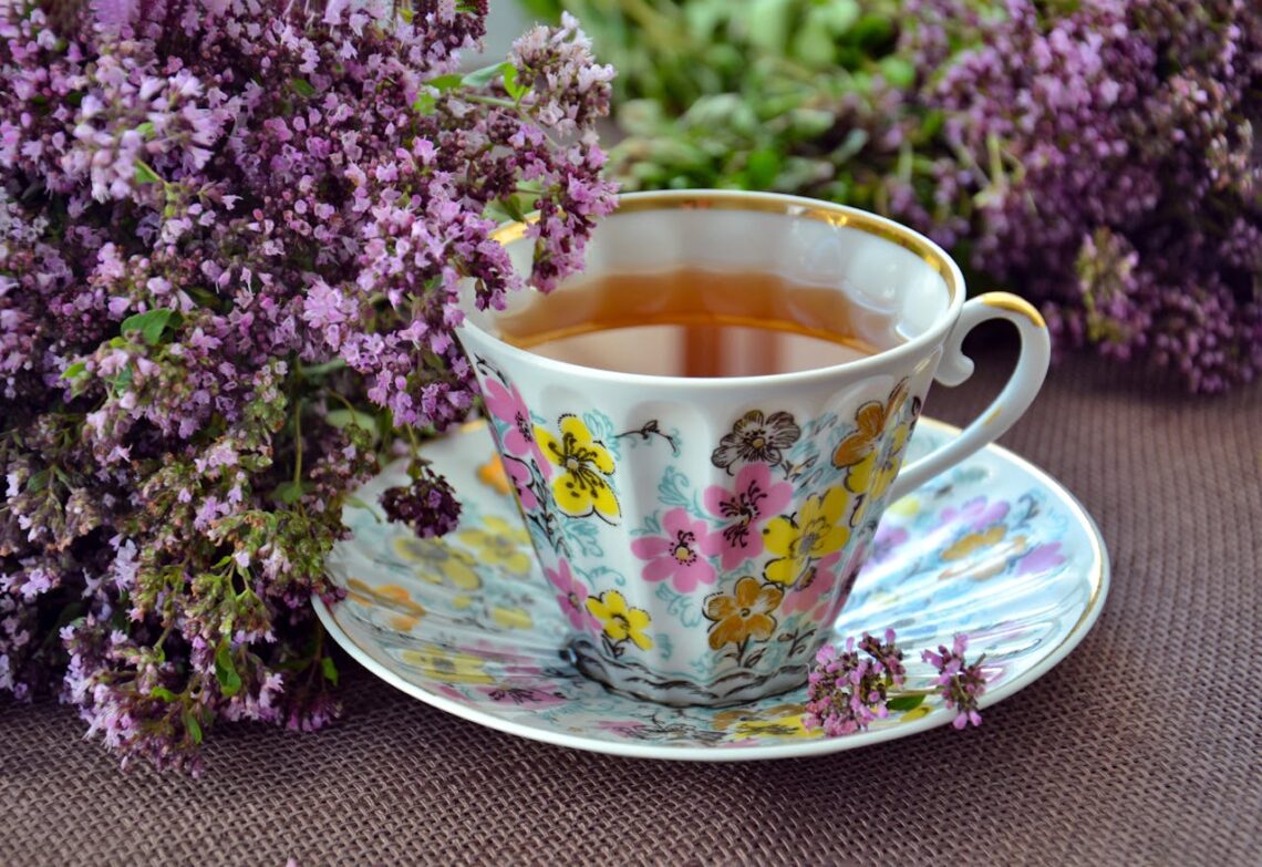 A cup of tea with purple flowers next to it.