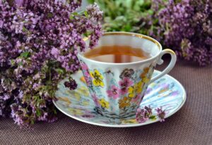 A cup of tea with purple flowers next to it.