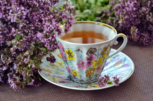 A cup of tea with purple flowers next to it.