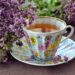 A cup of tea with purple flowers next to it.